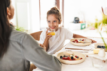 Wall Mural - image of attractive family mother and little daughter having breakfast at home in morning