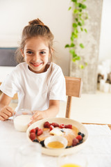 Wall Mural - Portrait of cute little girl drinking milk while having breakfast in morning at home