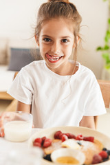Wall Mural - portrait of caucasian little girl drinking milk while having breakfast in morning at home