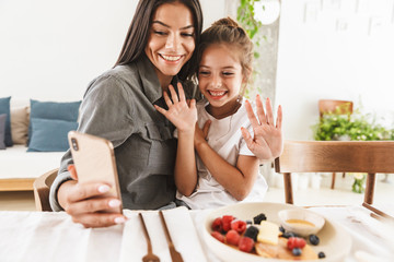 Wall Mural - image of attractive family mother and little daughter using cellphone together while having breakfas