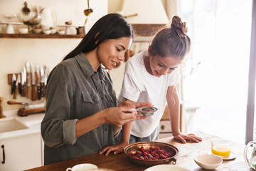Wall Mural - image of happy family woman and her little daughter cooking together meal with raspberry at cozy apa