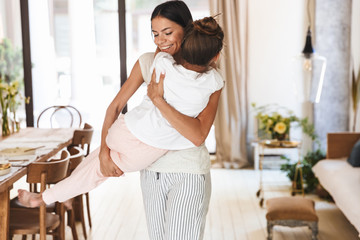 Wall Mural - image of happy family brunette mother smiling and holding her little daughter in hands at bright apa