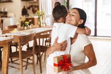 Wall Mural - image of positive family brunette mother smiling and giving present box to her little daughter at ho