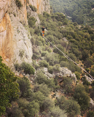 A man is walking along a stretched sling. Highline in the mountains. Man catches balance. Performance of a tightrope walker in nature. Highliner on the background of valley.