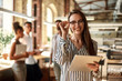 © Kostiantyn - Successful business woman. Young cheerful woman holding digital tablet and looking at camera with smile while standing in the modern office