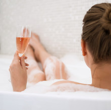 Woman With Glass Of Wine Is Relaxing In Bathtub. Rear View.