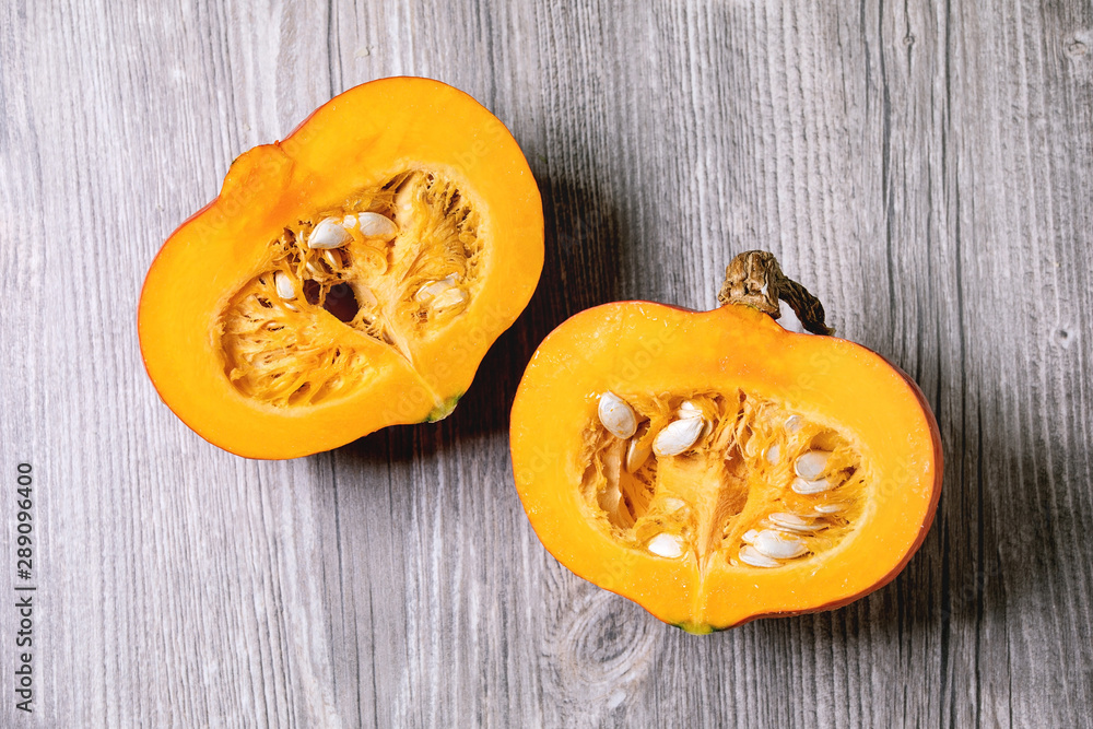 Two halves of raw organic hokkaido pumpkin with seeds over grey wooden background. Flat lay, space - obrazy, fototapety, plakaty 