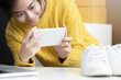asian girl using smartphone to shoot white sneaker posted for sale on the internet.startup small business owner working with tablet at workplace.happy owner & seller check product order to customer