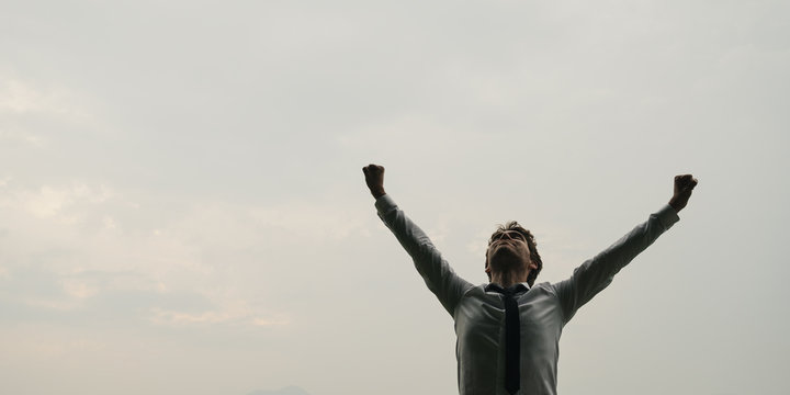 businessman standing under sky with his arms raised