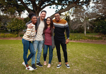 Wall Mural - Smiling group of friends in fashionable casual clothing standing together in park outdoors smiling and very happy - looking at camera 