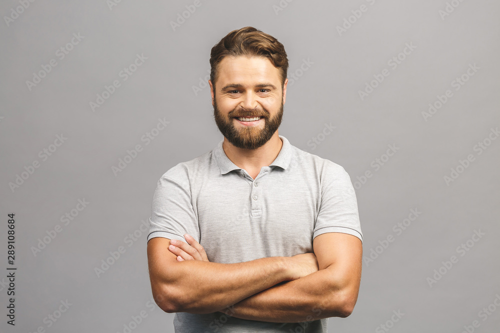 Happy young man. Portrait of handsome young man in casual shirt keeping arms crossed and smiling while standing against grey background - obrazy, fototapety, plakaty 