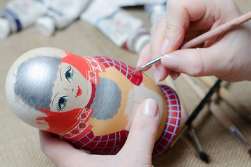 The artist draws a doll-matryoshka. Female hands with a brush close-up.