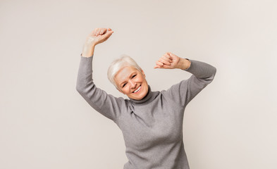 Positive aged lady dancing over light studio background