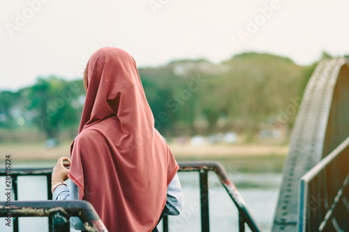Fotomural Back view of Muslim woman relax and admire the beautiful scenery in the evening on The Bridge of the River Kwai in Kanchanaburi, Thailand