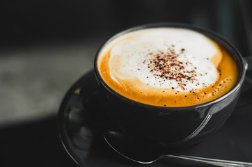 close up modern hot black coffee the cappuccino on dark background with coffee bubble foam pattern and texture in black cup looking and feel so delicious on glasses table in coffee shop.