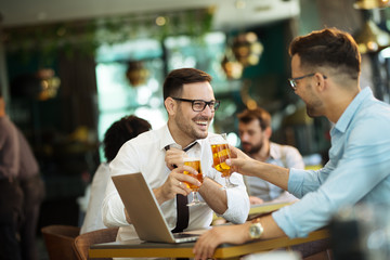 Two young businessmen use a laptop and drink beer