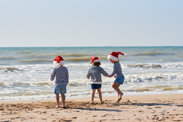 Happy Little children travelers in Santa hats having fun on tropical beach. Christmas and new year holiday vacation concept. 