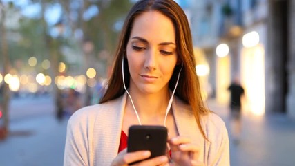 Wall Mural - Front view portrait of a woman walking listening to music at evening in the street