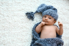 Cute Little Baby In Grey Hat And Plaid Lying On Soft Blanket, Top View. Space For Text