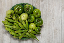 Fresh Organic Green Tomatoes And Okra In A Basket Isolated On A White Wood Board.