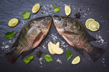 Wall Mural - Tilapia fish freshwater and ginger lemon lime herb spices vegetable for cooking food in the asian restaurant - Fresh raw tilapia on black background