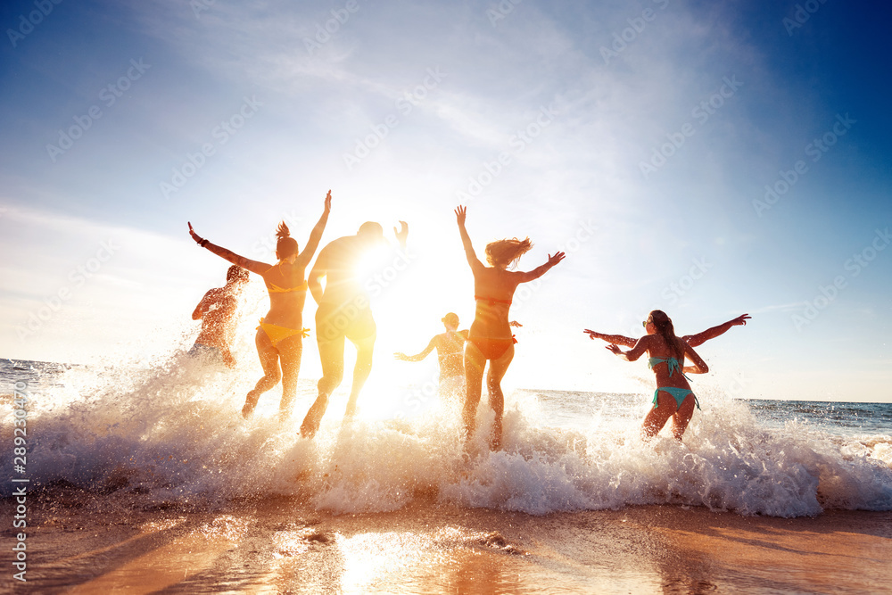 Big group happy friends runs and having fun at sunset beach - obrazy, fototapety, plakaty 