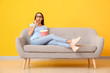 Young woman with popcorn watching movie on sofa near color wall