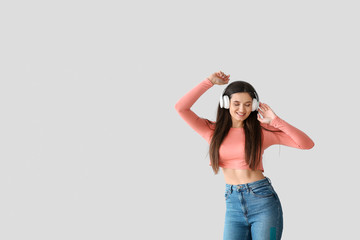 Poster - Beautiful young woman listening to music and dancing against light background