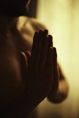 Authentic vertical close up shot of namaste gesture. Man practicing yoga in dark intimate atmosphere, holding two hands together. Film grain effect. Handsome athletic body in motion captured indoors.