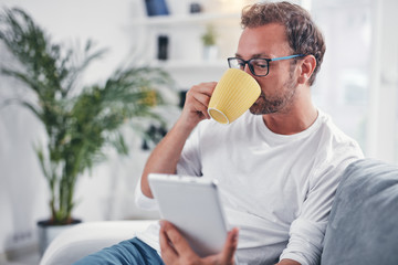 Man holding tablet, surfing online and drinking coffee.