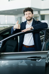 Perfect car. Happy mature male buyer showing thumbs up leaning on his new car at the dealership