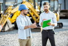 Builder Choosing Heavy Machinery For Construction With A Sales Consultant Standing With Some Documents On The Open Ground Of A Shop With Special Vehicles