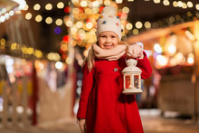 Holidays, Childhood And People Concept - Happy Little Girl With Lantern At Christmas Market In Winter Evening