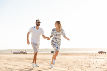 Wall Mural - Photo of caucasian happy couple smiling and running on sunny beach