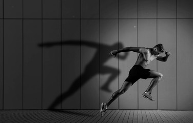 athletic man sprinter running on dark wall background