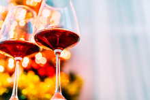 Two Glass Of Red Wine In Front Of Christmas Tree Lights Bokeh. New Year Eve And Xmas Celebration Party.