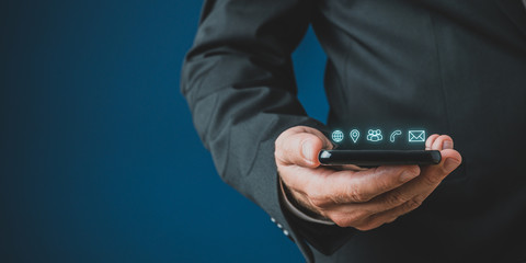 Fototapete - Businessman holding mobile phone with contact and communication icons glowing above it
