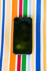 Wall Mural - Black smartphone on a multi-colored fabric. The surface of a multi-colored cotton with a black smartphone on it