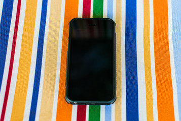 Wall Mural - Black smartphone on a multi-colored fabric. The surface of a multi-colored cotton with a black smartphone on it