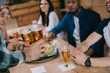 © LIGHTFIELD STUDIOS - cropped view of man holding glasses of light beer near multicultural friends in pub