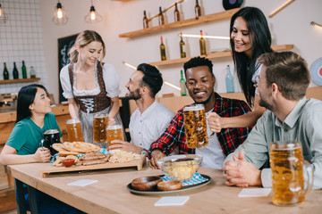 Wall Mural - two attractive waitresses serving beer for multicultural friends in pub