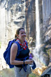 © dabyg - Young woman stands in-front of a waterfall in Yosemite National Park, with her water bottle for hydration.