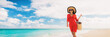 Luxury beach vacation elegant lady walking on beach stroll with beachwear sun hat and straw tote bag wearing red cover-up dress panoramic banner.