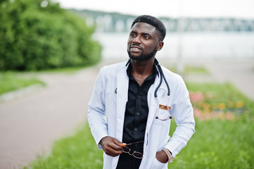 Wall Mural - Young african american male doctor in white coat with a stethoscope posed outdoor.