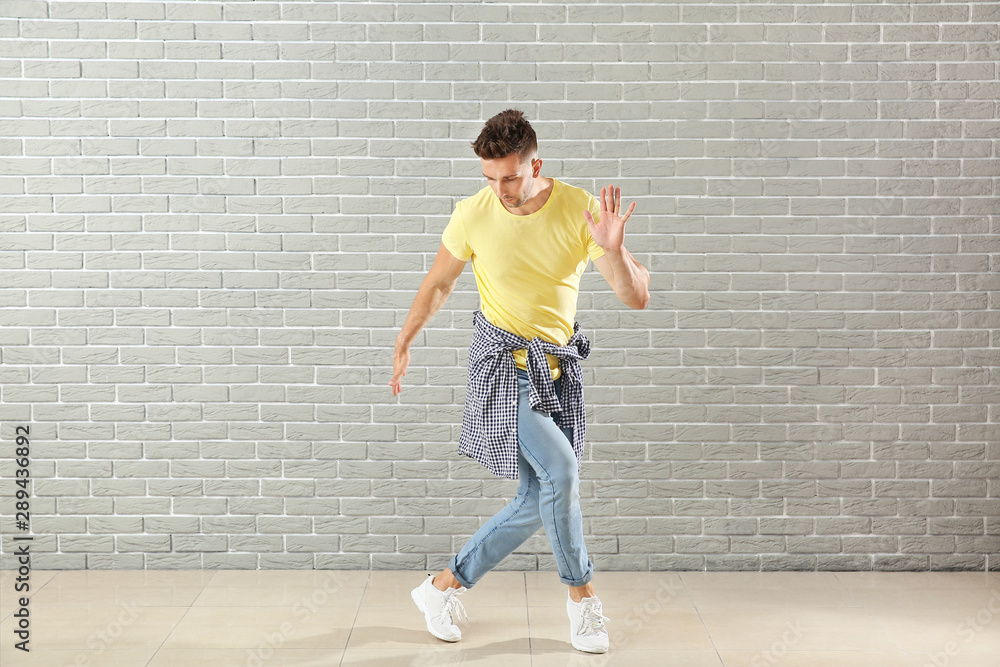 Handsome young man dancing against brick wall