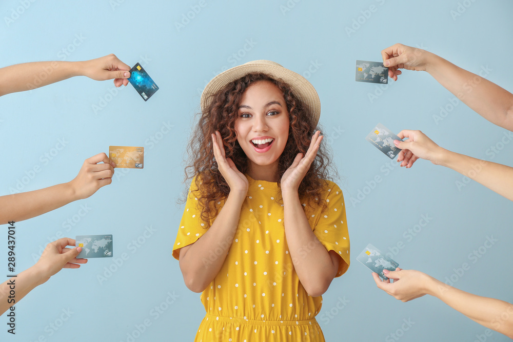 Young African-American woman and hands with credit cards on color background - obrazy, fototapety, plakaty 