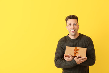 Poster - Handsome young man with gift on color background