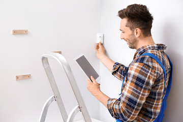 Wall Mural - Electrician with tablet computer installing alarm system indoors