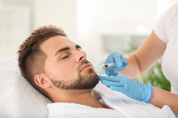 Handsome man receiving filler injection in beauty salon