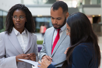 Serious business colleagues with papers. Multiethnic young business people standing together and looking at folder with documents. Business concept